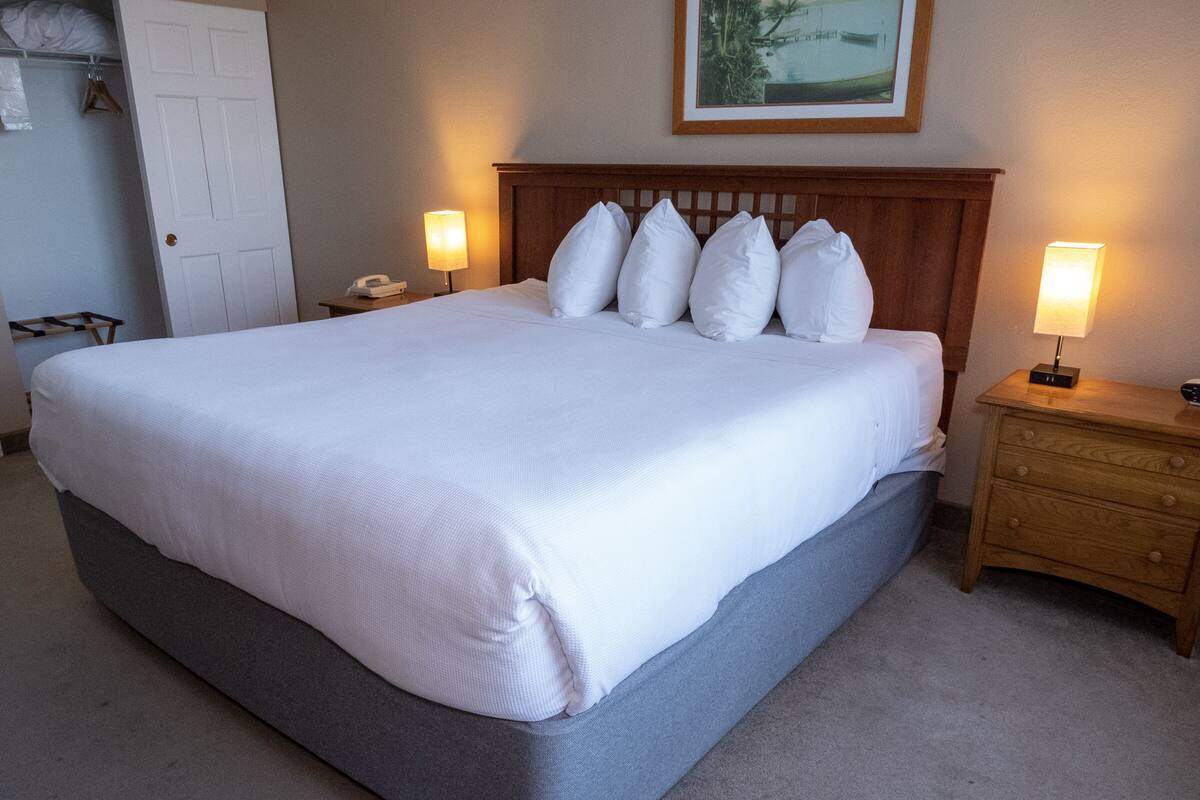 A neatly made bed with a wooden headboard, a bedside table with a lamp, and a framed picture on the wall.