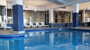 An indoor swimming pool with blue-tiled edges, lounge chairs, and a clear view of the interior. - Delavan Lake Resort (Delavan)