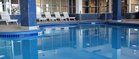 An indoor swimming pool with blue-tiled edges, lounge chairs, and a clear view of the interior.