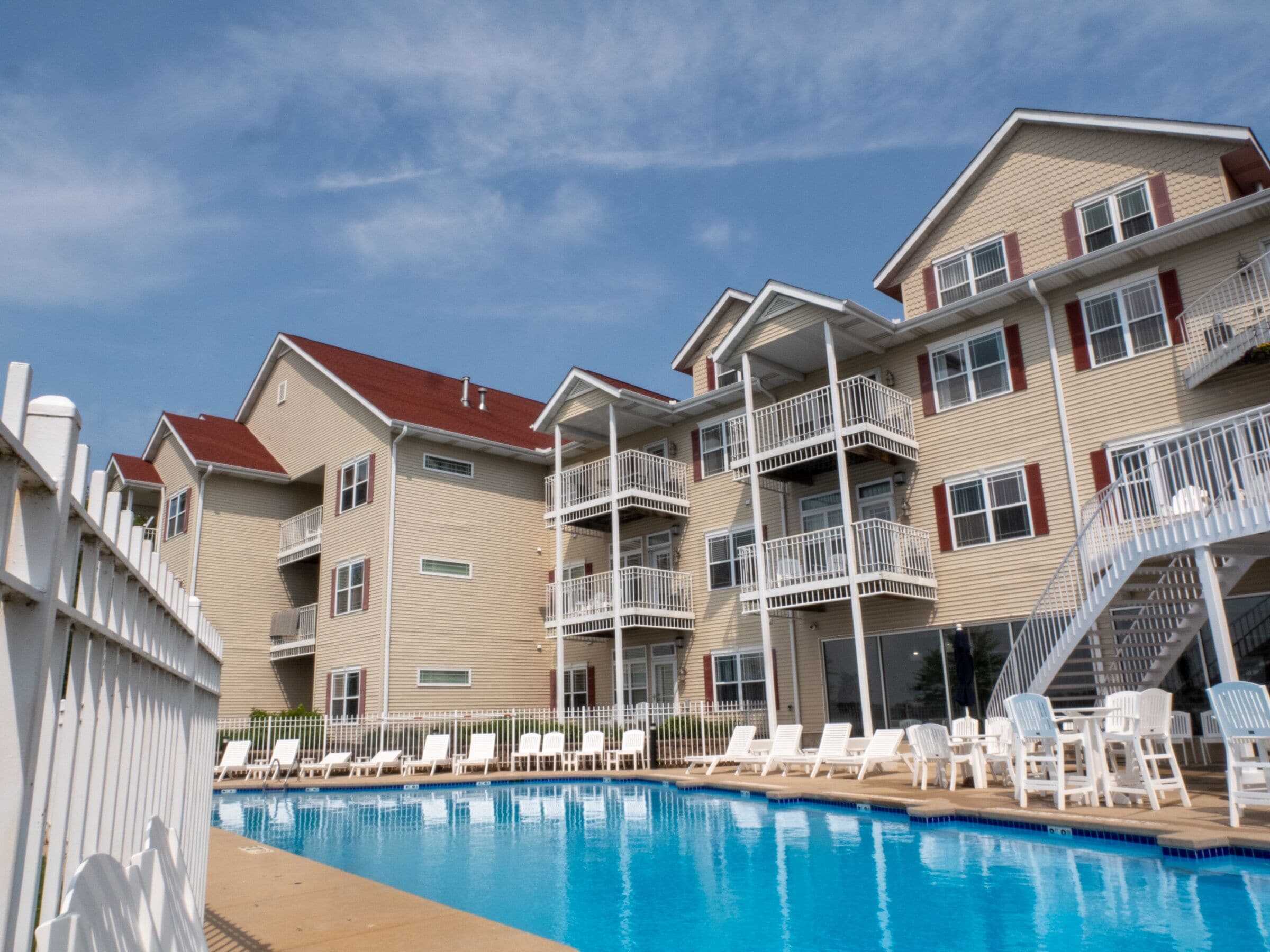 A hotel with a swimming pool, multiple balconies, and a white fence.