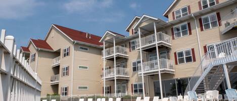 A hotel with a swimming pool, multiple balconies, and a white fence.