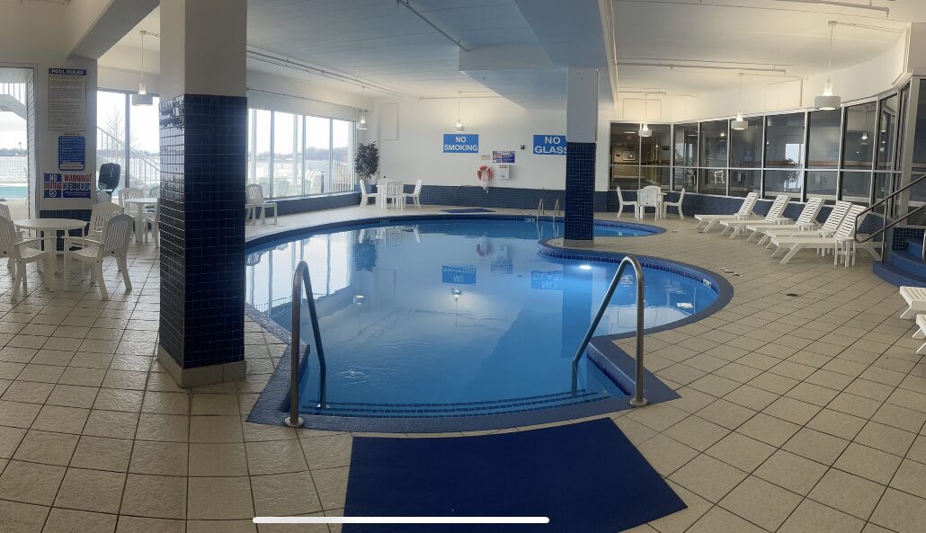 Une piscine intérieure dotée d’une signalisation claire, de chaises longues et offrant une vue sur l’extérieur grâce à de grandes fenêtres.