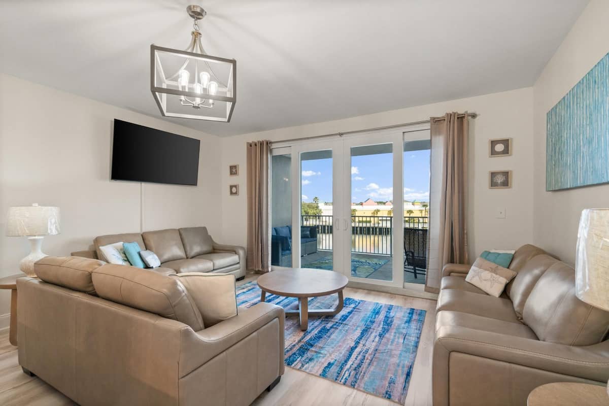 A modern living room with a beige sofa set, a round coffee table, and a flat-screen TV mounted on the wall.