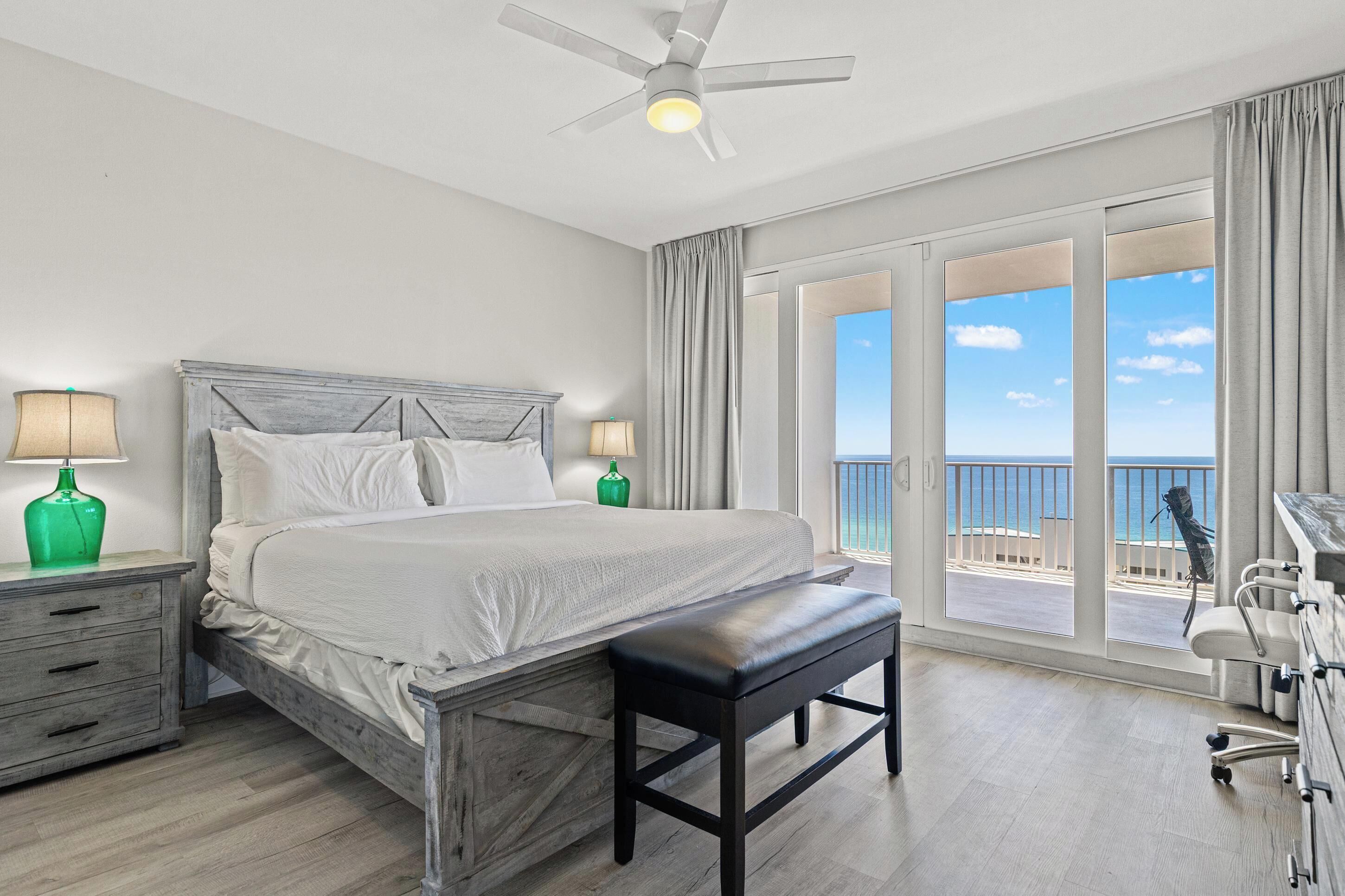 Ein Hotelzimmer mit Bett, Nachttischlampen, einer Bank, einem Schreibtisch und Blick aufs Meer.