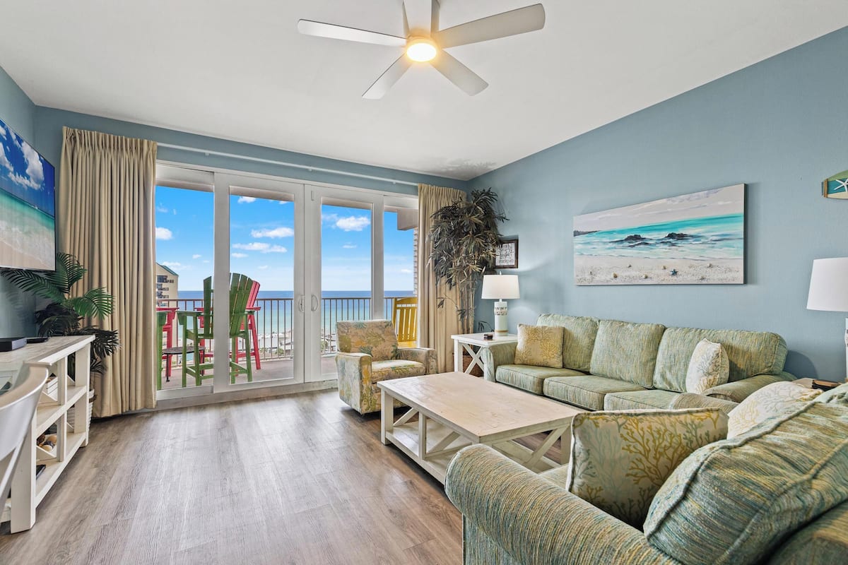 A spacious living room with a balcony, a ceiling fan, and a view of the ocean.