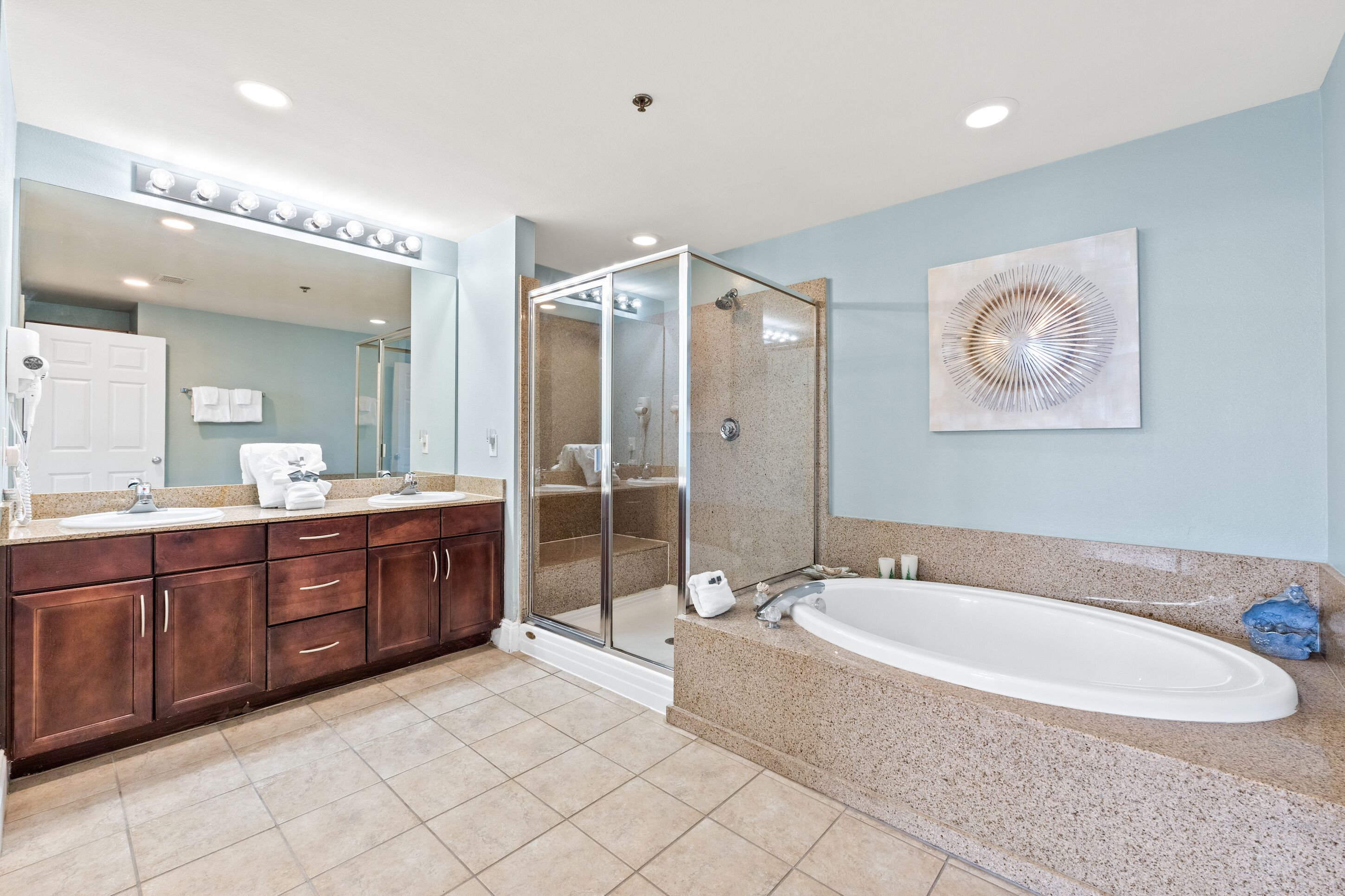 Une salle de bain moderne dotée d’une douche à parois de verre, d’une grande baignoire et d’un meuble-lavabo avec un miroir et des luminaires.