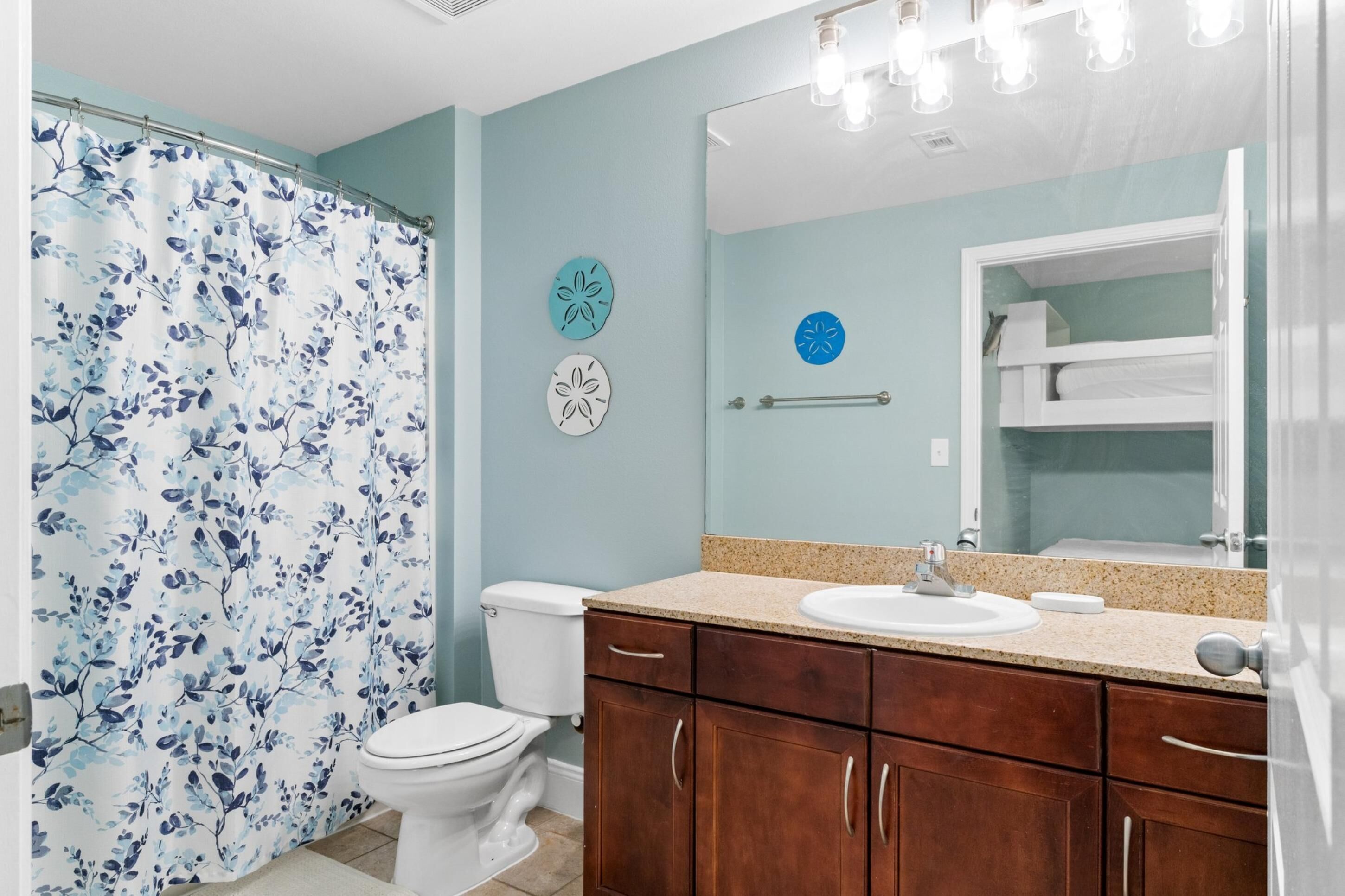 A bathroom with a shower curtain, toilet, vanity with a sink, and a mirror.
