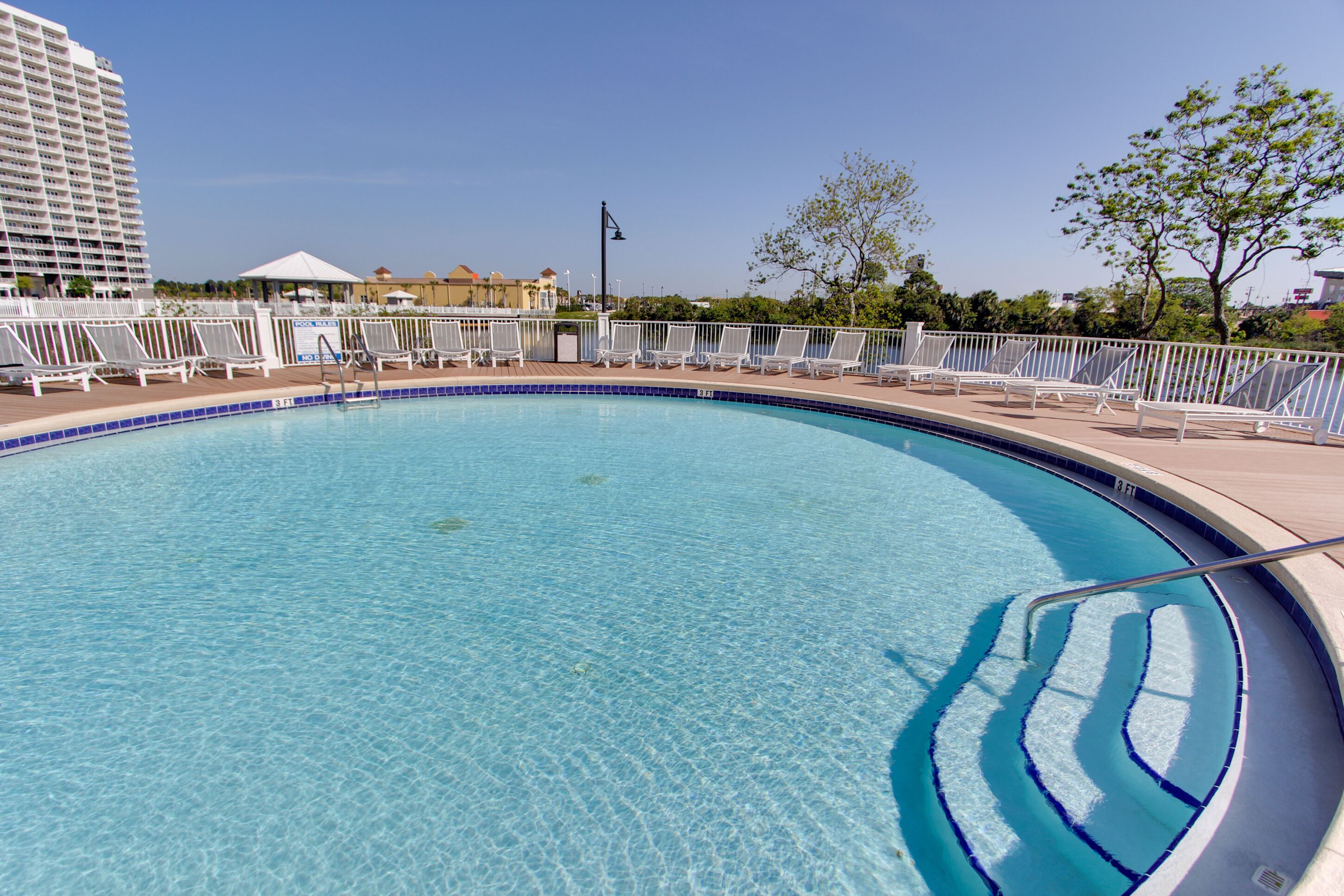 Une piscine d’un bleu éclatant, bordée de chaises longues blanches et entourée d’une clôture blanche.