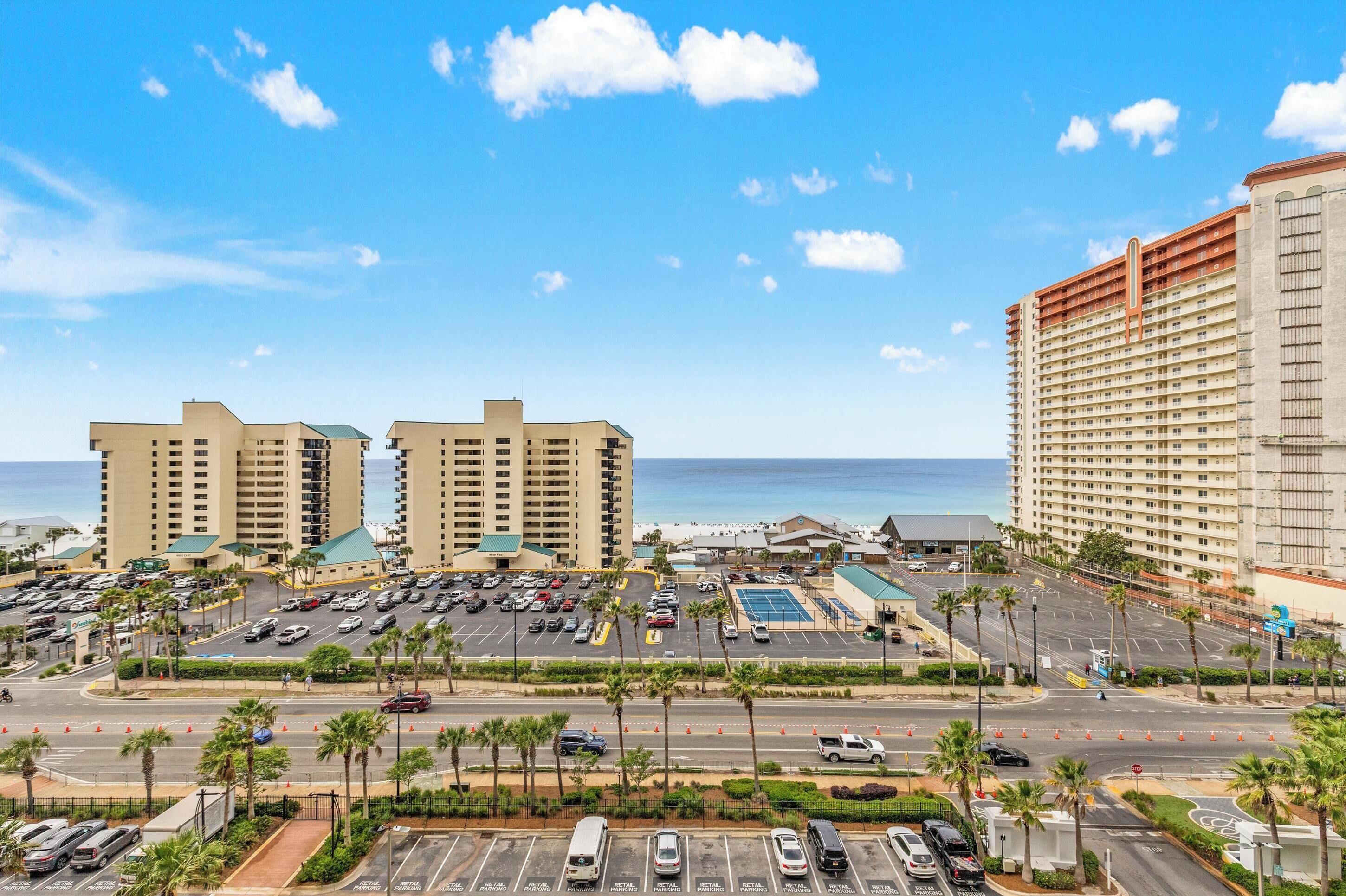 A coastal hotel complex with multiple high-rise buildings, a parking lot, and a view of the ocean.