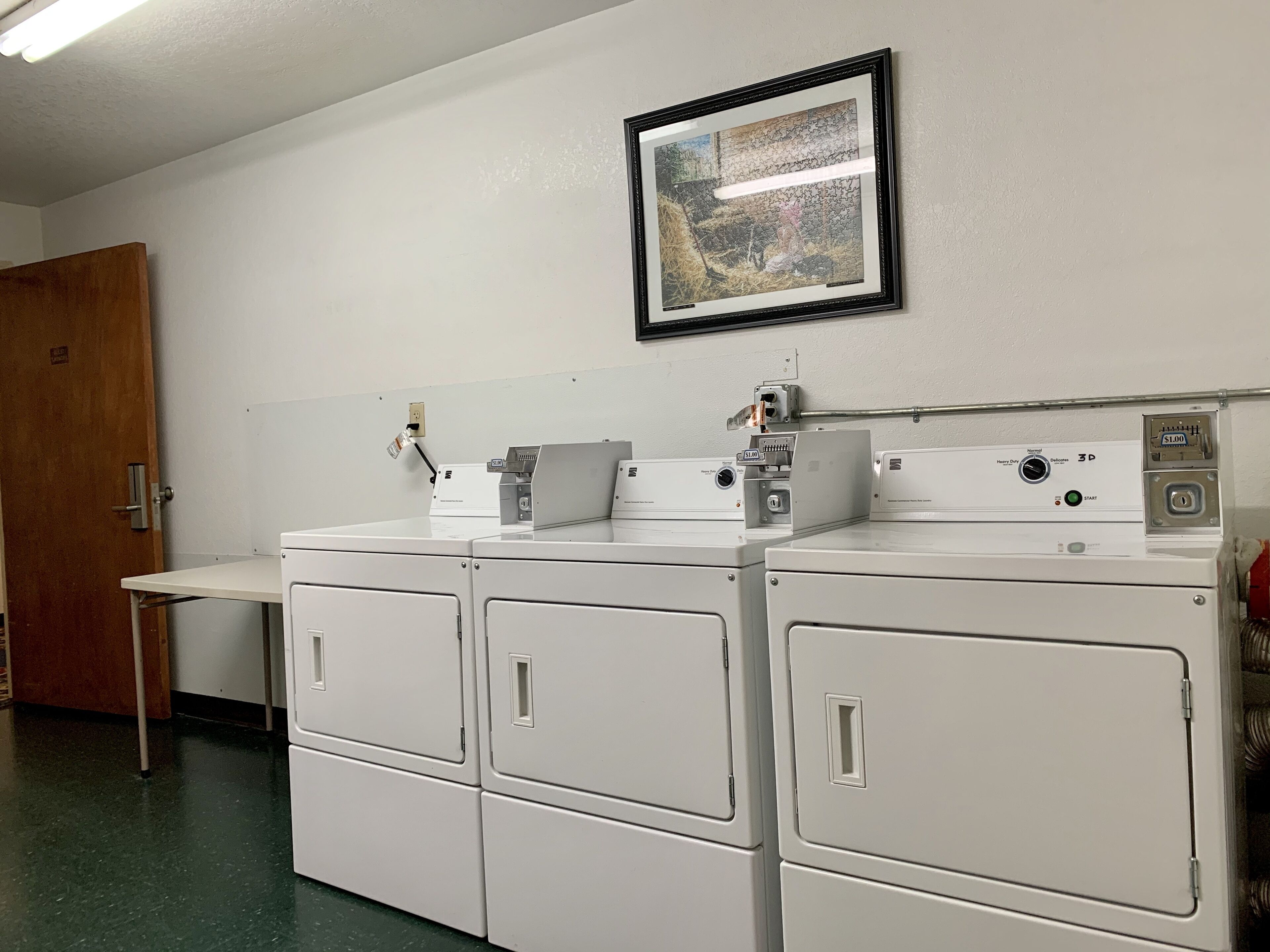 A laundry room with stacked washers and dryers, a framed picture on the wall, and a door to the left.