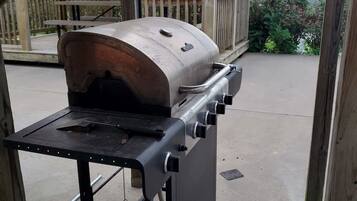 A portable barbecue grill with a metal grate and control knobs, positioned on a concrete surface under a wooden pergola.
