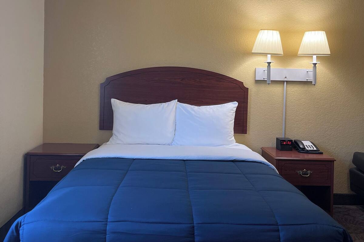 Ein Hotelzimmer mit einem Bett, zwei Nachttischlampen, einem Nachttisch mit Telefon und einer Wanduhr.