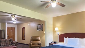 A hotel room with a bed, a chair, a sofa, a ceiling fan, and a nightstand with a lamp. - Candlelight Inn & Suites Hwy 69 near McAlester (McAlester)