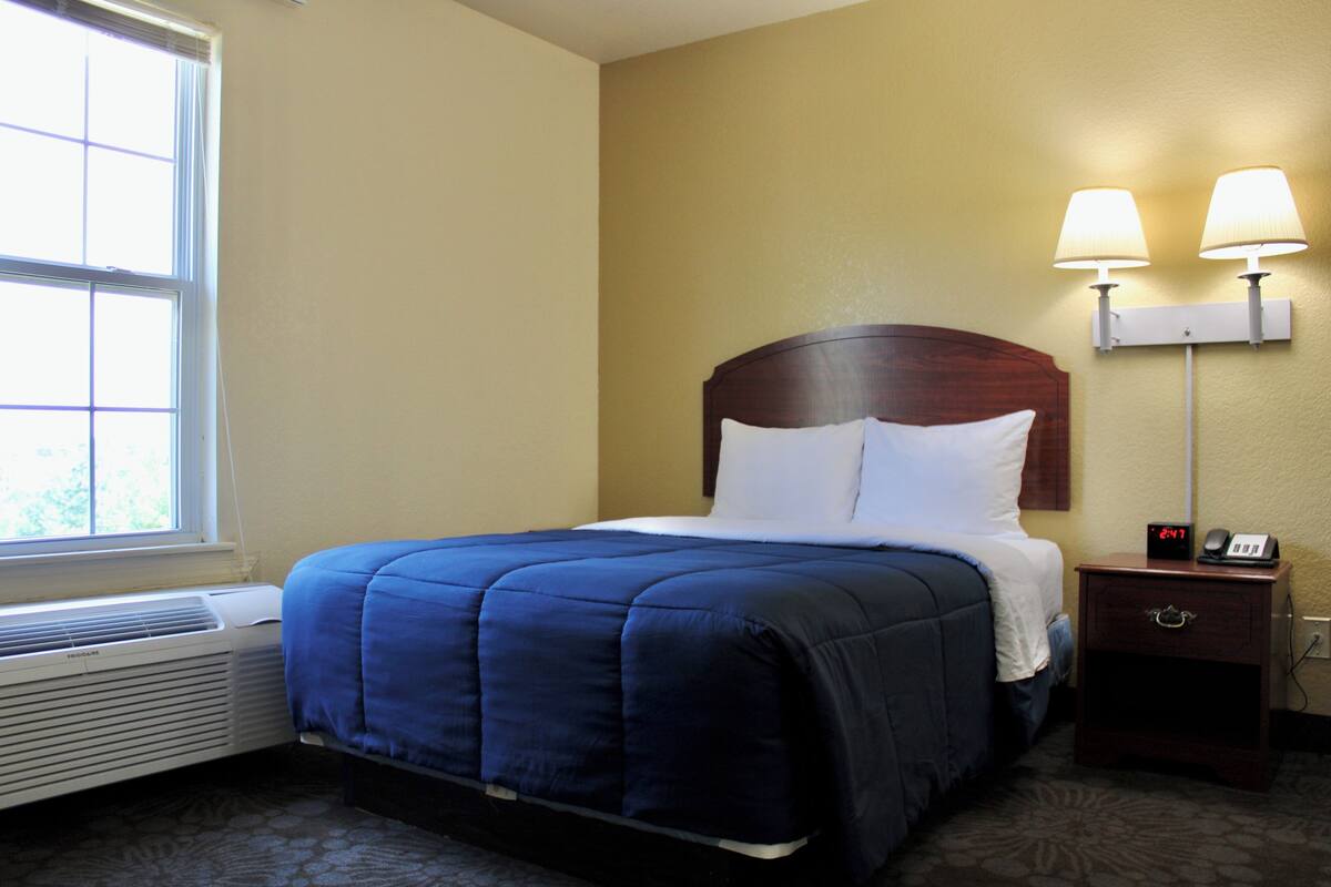 Ein Hotelzimmer mit einem Bett, einem Nachttisch mit Lampe, einem Heizgerät und einem Fenster.