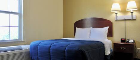 A hotel room with a bed, a nightstand with a lamp, a heater, and a window.