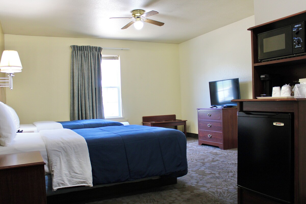 A hotel room with a bed, a desk, a television, a refrigerator, and a ceiling fan.