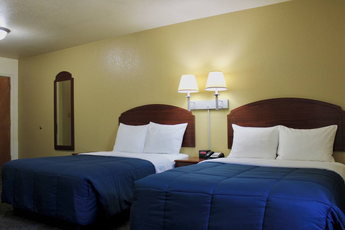 Ein Hotelzimmer mit zwei Betten, jeweils mit einem hölzernen Kopfteil, weißer Bettwäsche und einem Nachttisch mit Lampe.