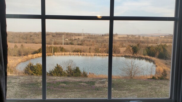 A view through a window with a grid pattern, featuring a body of water, grassy fields, and distant power lines. - Candlelight Inn & Suites Hwy 69 near McAlester (McAlester)
