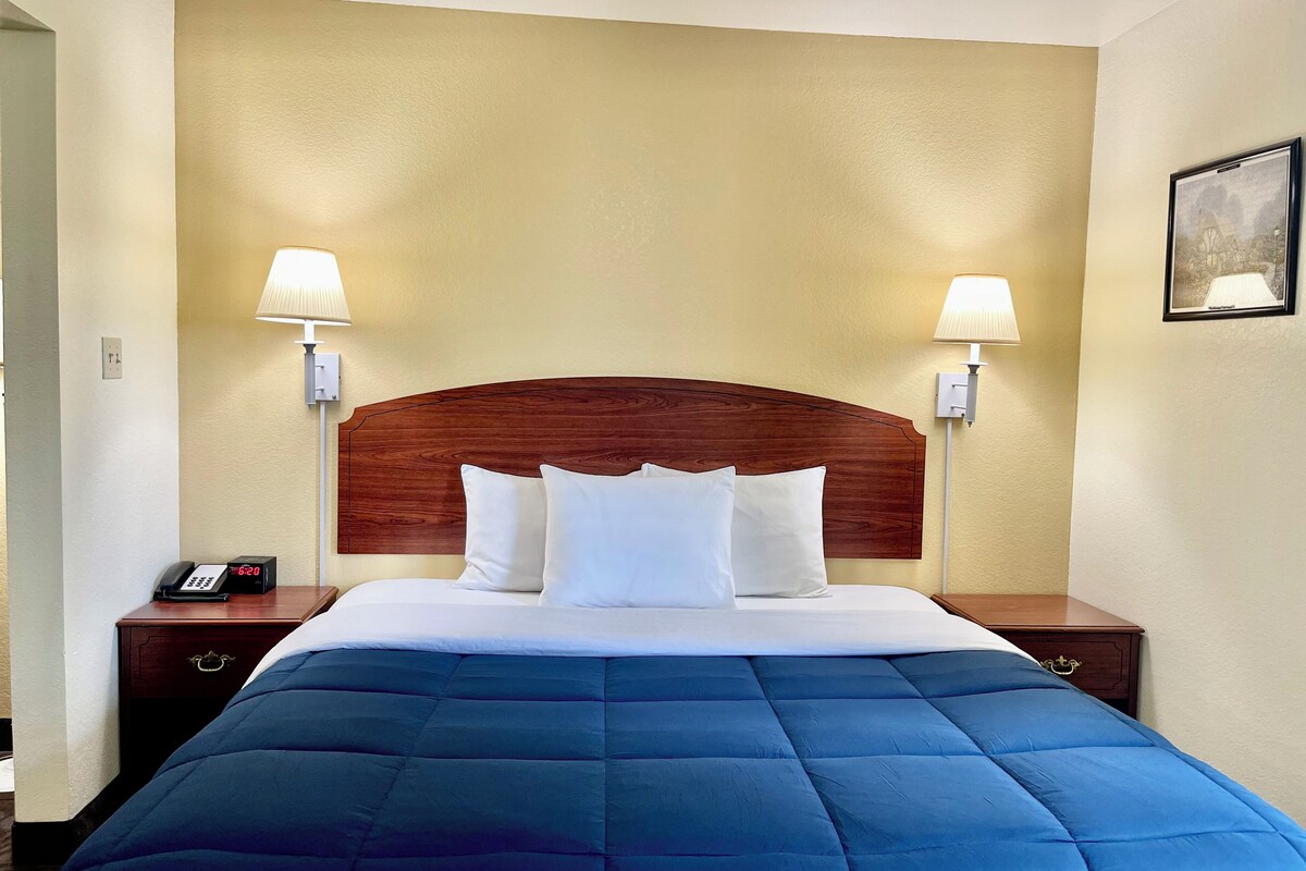 A hotel room with a large bed, two bedside lamps, a nightstand with a phone, and a framed picture on the wall.