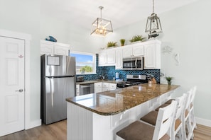 A modern kitchen with white cabinets, stainless steel appliances, a granite island, and pendant lighting.