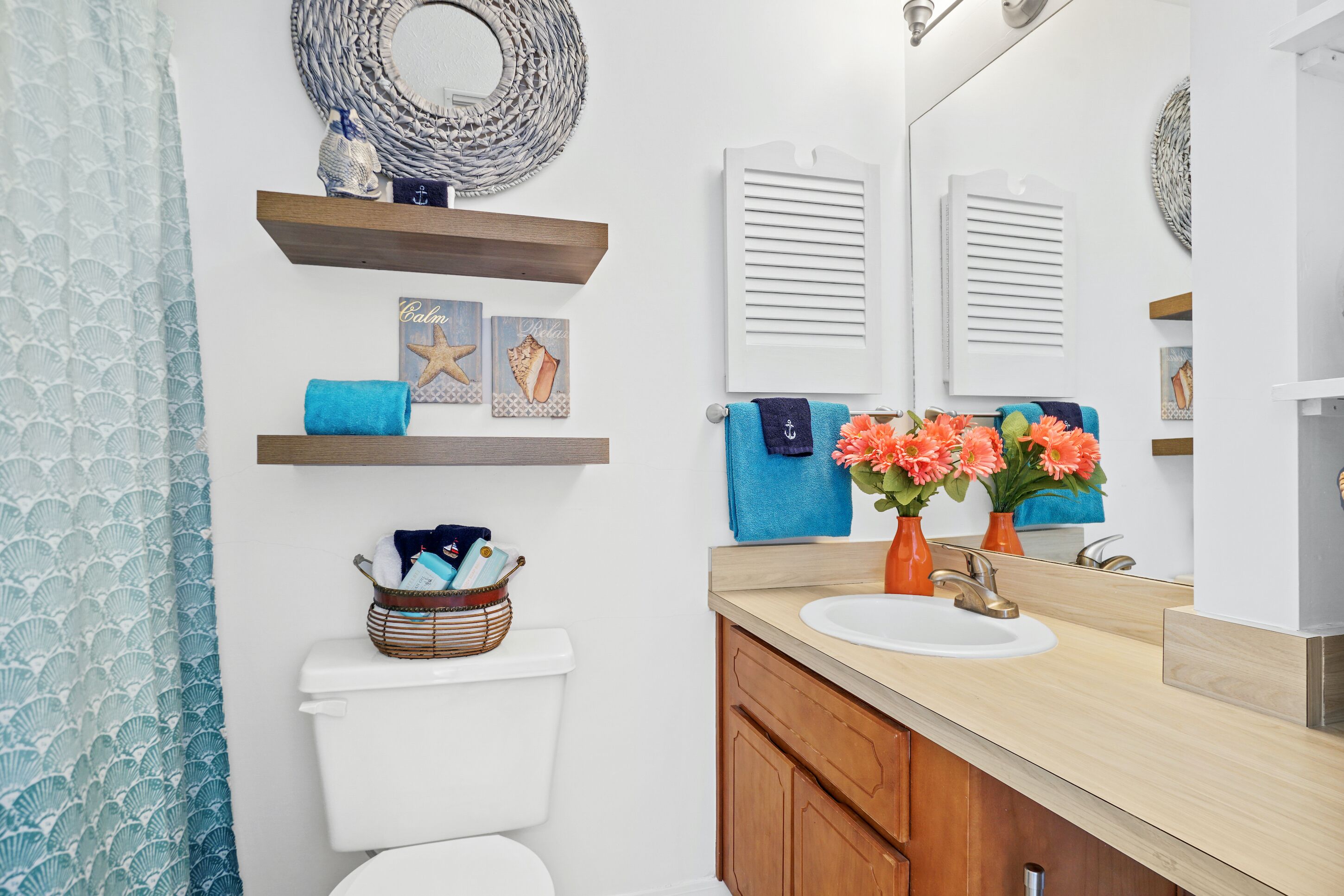 A bathroom with a toilet, a sink, wooden cabinets, a mirror, and decorative items including a starfish, a blue towel, and a basket of toiletries.