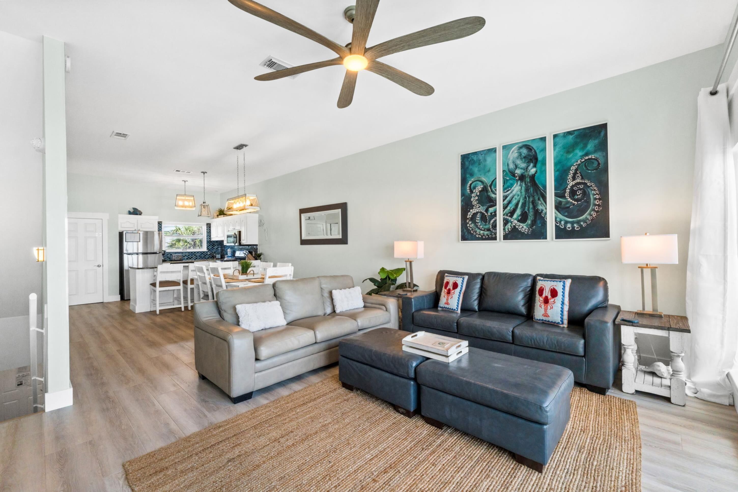 A modern living room with a sofa, ottoman, and a ceiling fan.