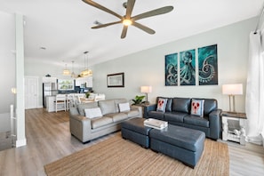 A modern living room with a sofa, ottoman, and a ceiling fan. - Beachside West Panama City Beach by Panhandle Getaways (Panama City Beach)