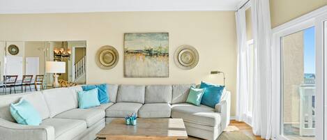 Uma sala de estar com um sofá seccional, uma mesa de centro e um quadro na parede.