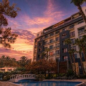 A multi-story hotel with a pool, surrounded by palm trees and a sunset sky. - K Tower Boutique Hotel By Lucerna (Tijuana)