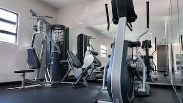 Un gimnasio con diferentes máquinas de ejercicio, una banca y un espejo grande.