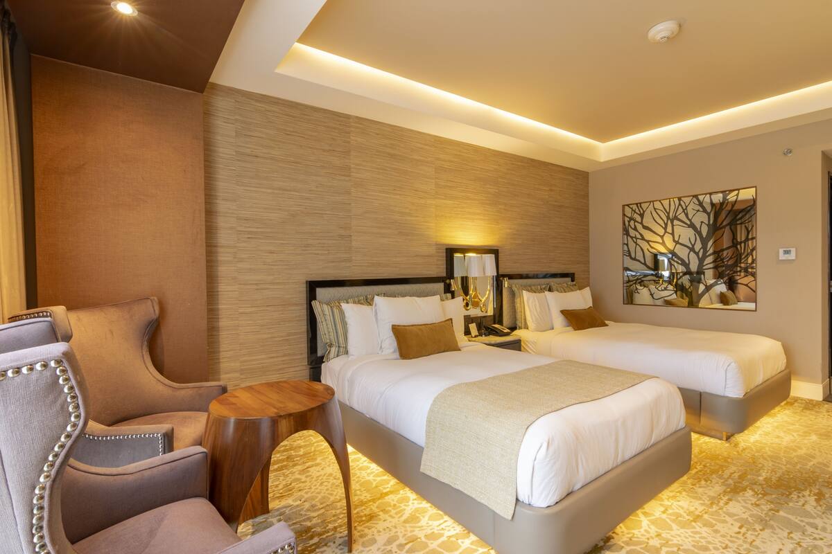 Een hotelkamer met twee bedden, een zithoek met een stoel, een bijzettafeltje en een decoratief wandobject.