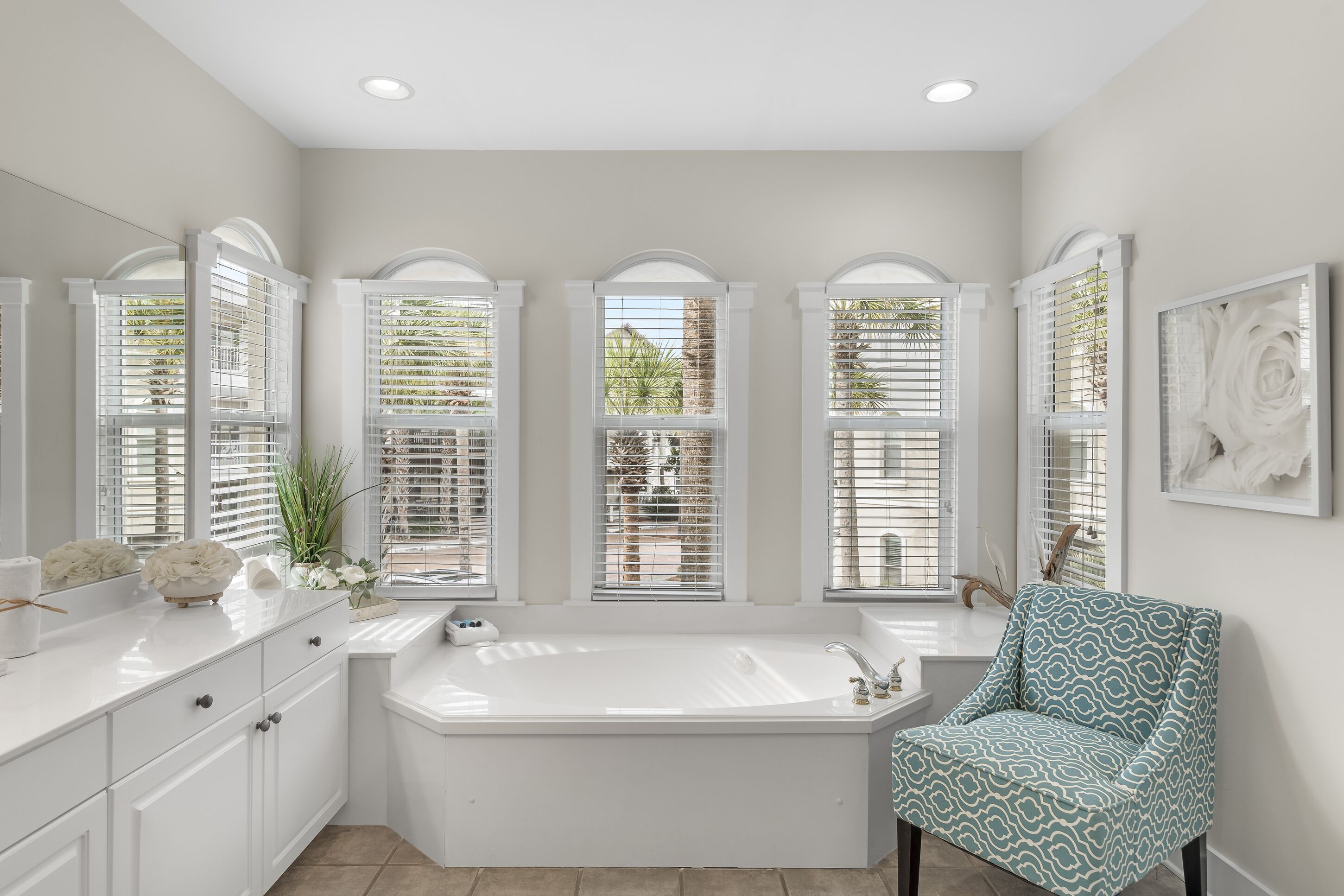 A bathroom with a large bathtub, white cabinetry, and a window with blinds.