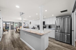 Una cocina moderna con armarios blancos, una isla de mármol, electrodomésticos de acero inoxidable y piso de madera.