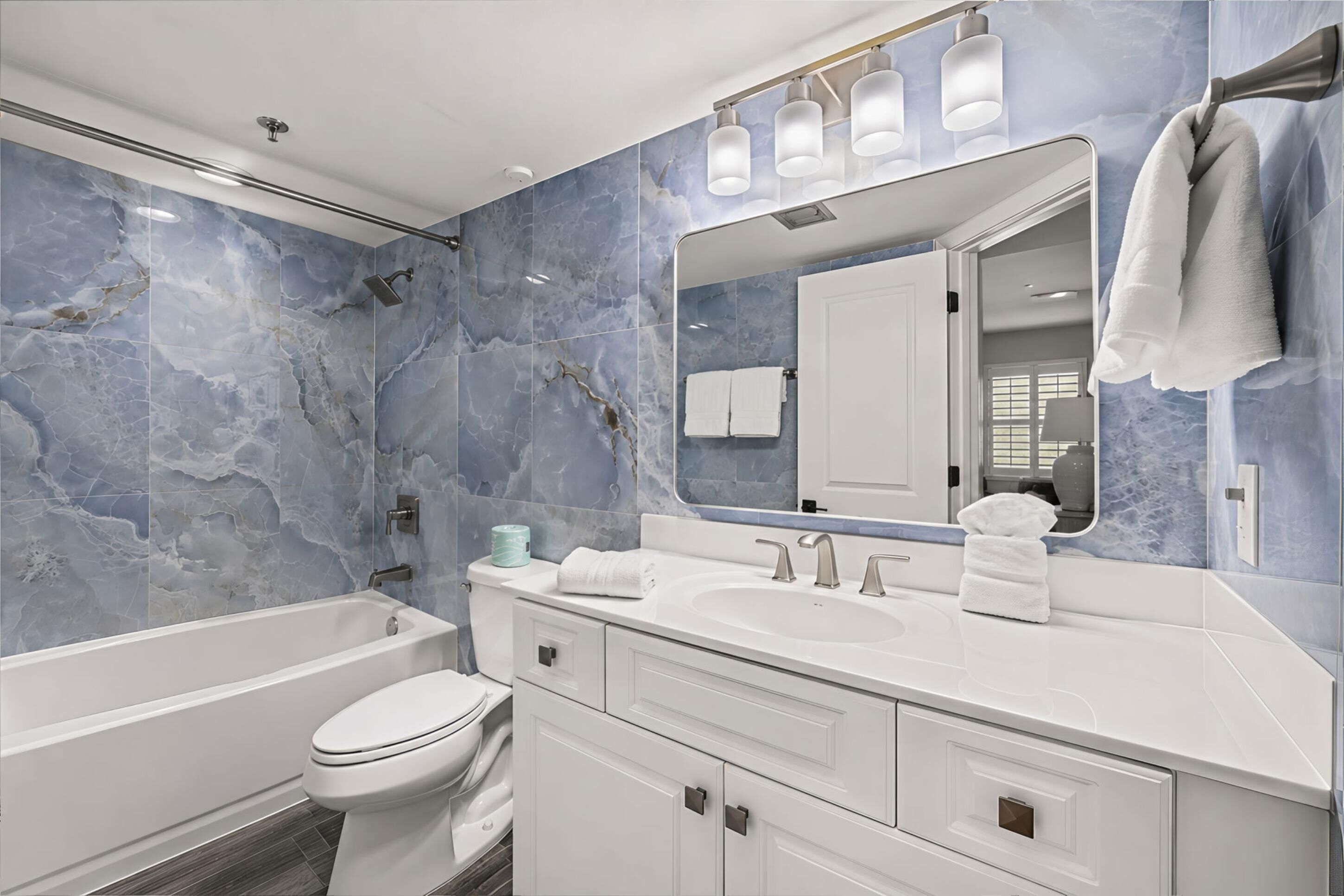 A modern bathroom with a bathtub, toilet, and vanity with a mirror and towel rack.