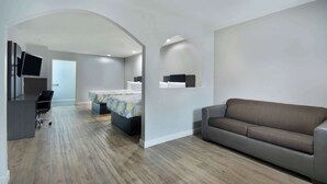 A modern living room with a sofa, a desk with a chair, a bed with a patterned bedspread, and a TV mounted on the wall. - Motel 6 Houston, TX - I-10 West (Houston)