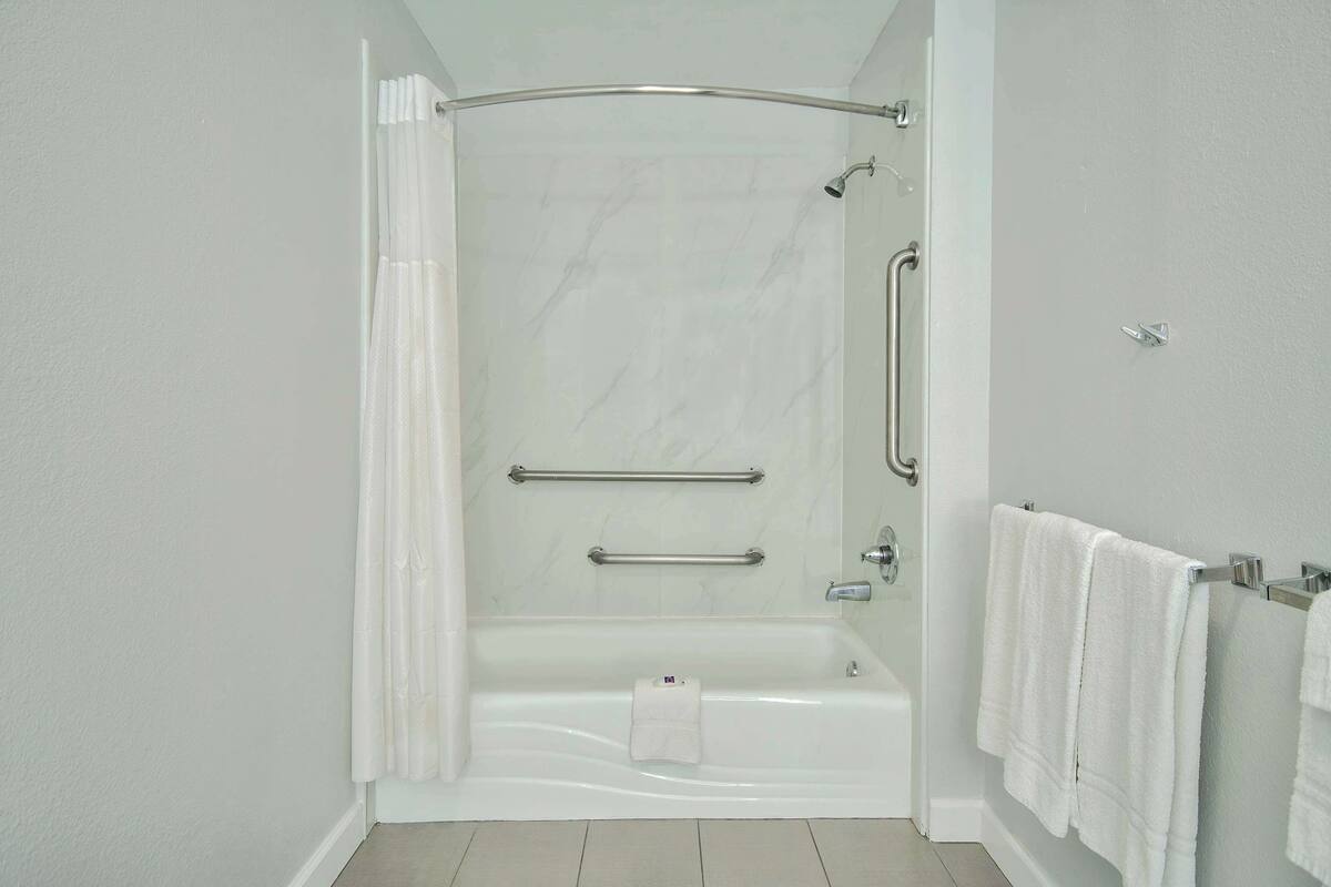 A modern bathroom with a walk-in shower, grab bars, and a towel rack.