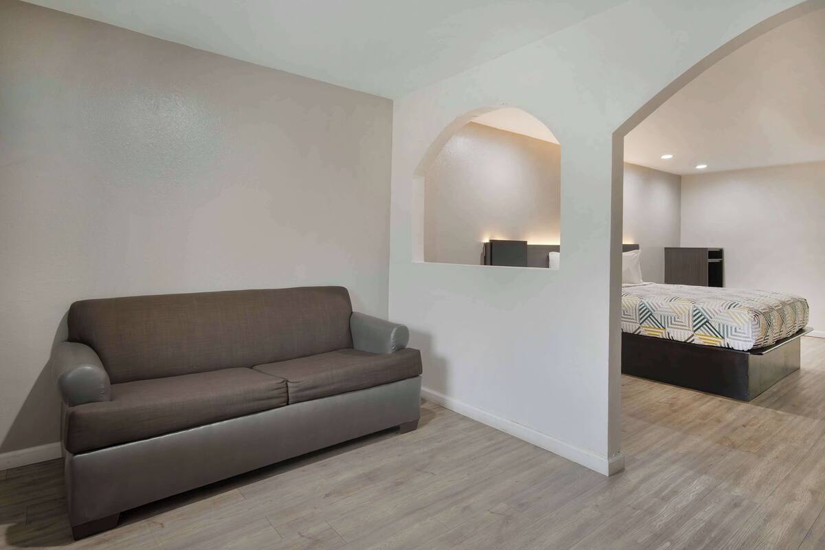A modern bedroom with a grey sofa, a bed with patterned bedding, and a mirror on the wall.