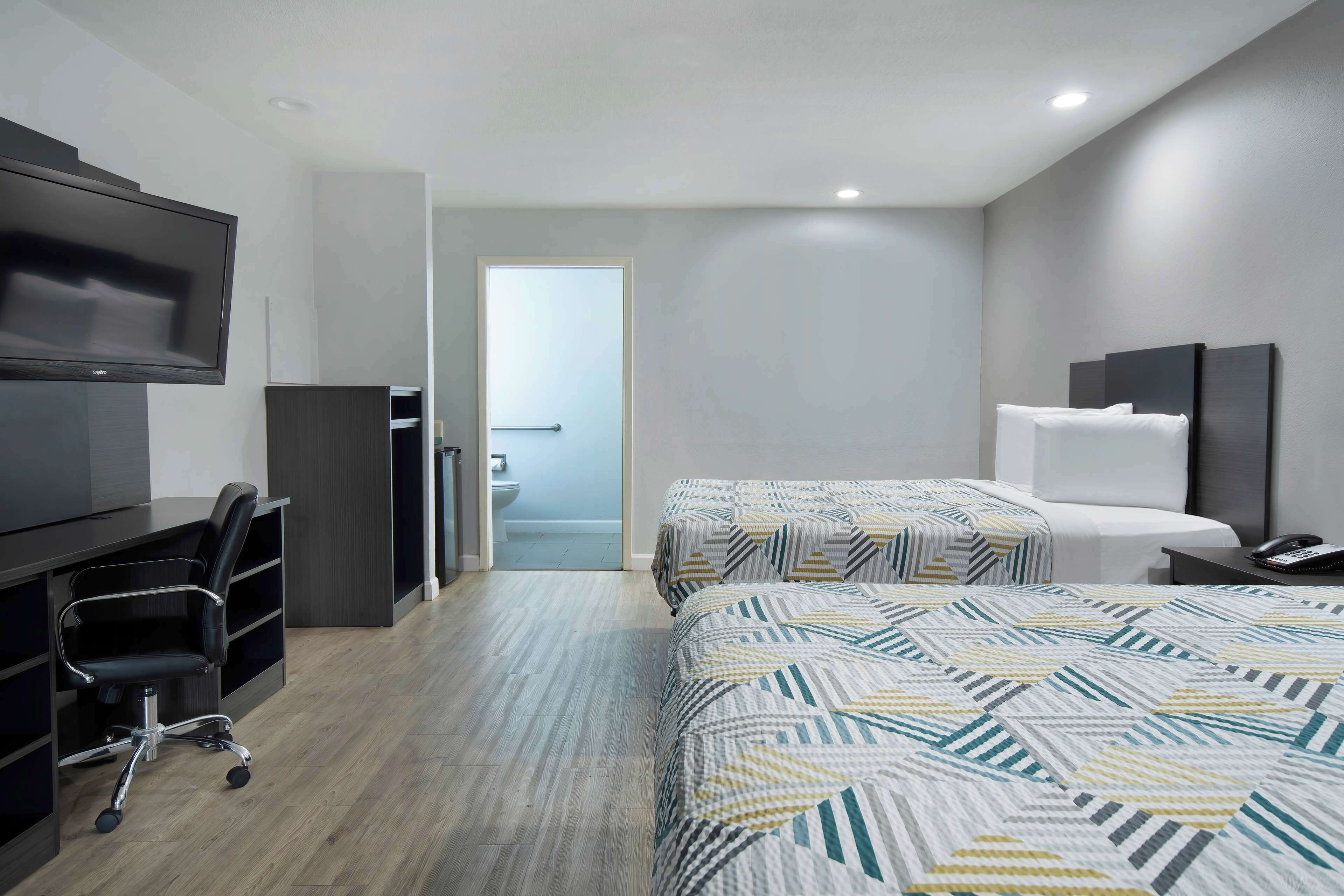 A hotel room with a desk, chair, two beds, and a television.