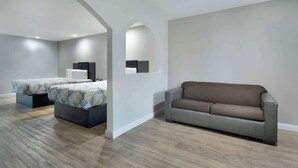 A modern living room with a sofa, a bed with patterned bedding, and a flat-screen TV on a stand. - Motel 6 Houston, TX - I-10 West (Houston)