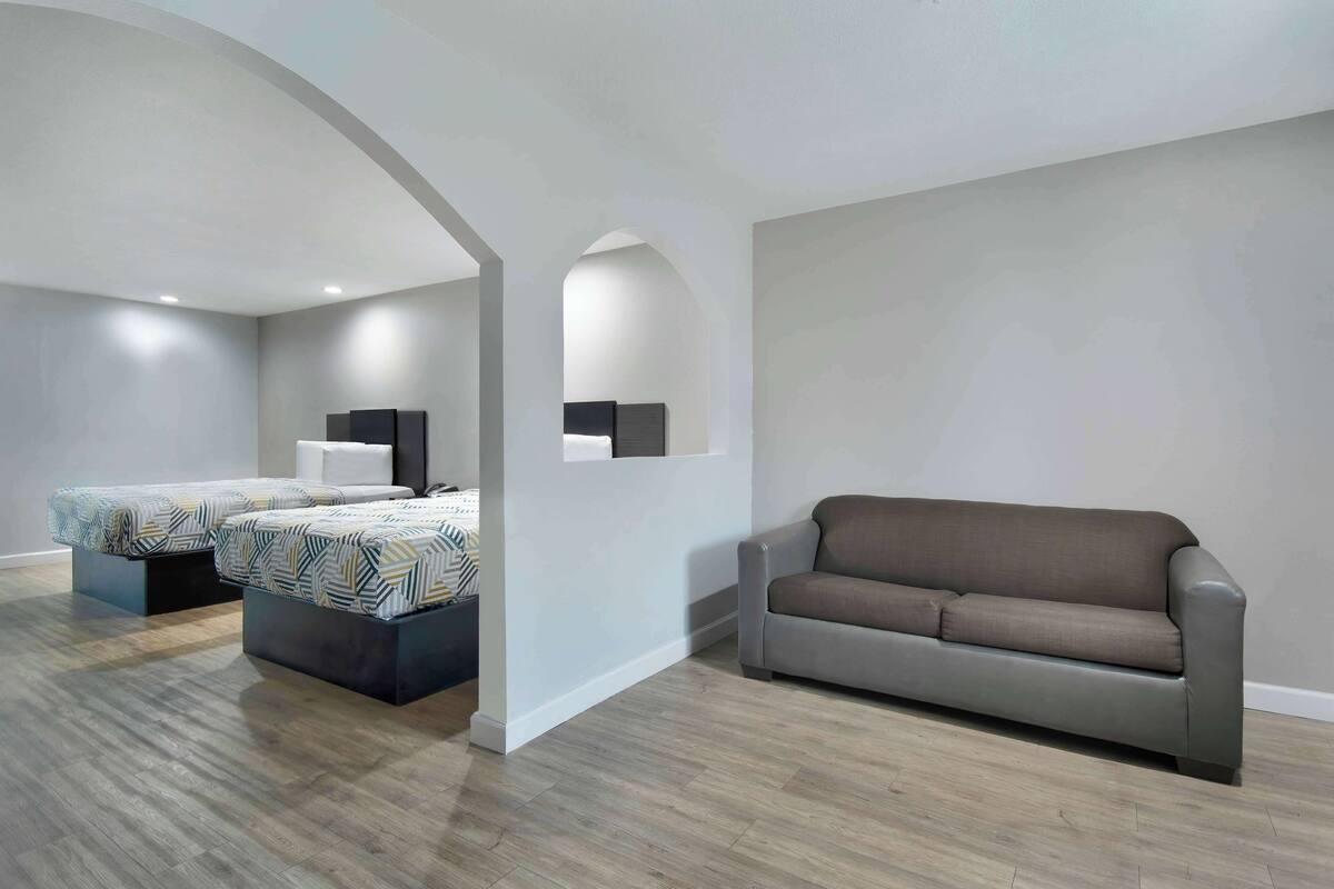 A modern living room with a sofa, a bed with patterned bedding, and a flat-screen TV on a stand.