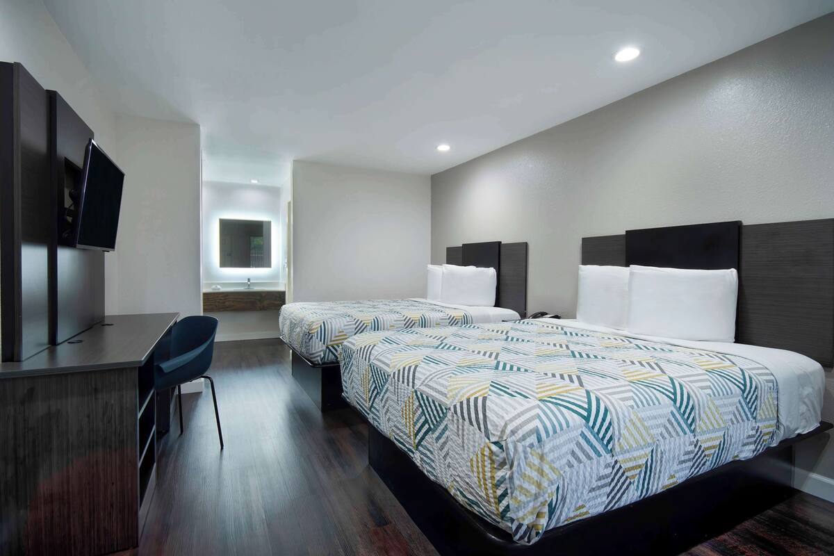 A hotel room with two beds, a desk, and a TV.