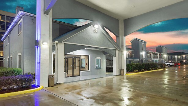 A hotel entrance with a covered waiting area, a clear sky, and a parking lot. - Motel 6 Houston, TX - I-10 West (Houston)