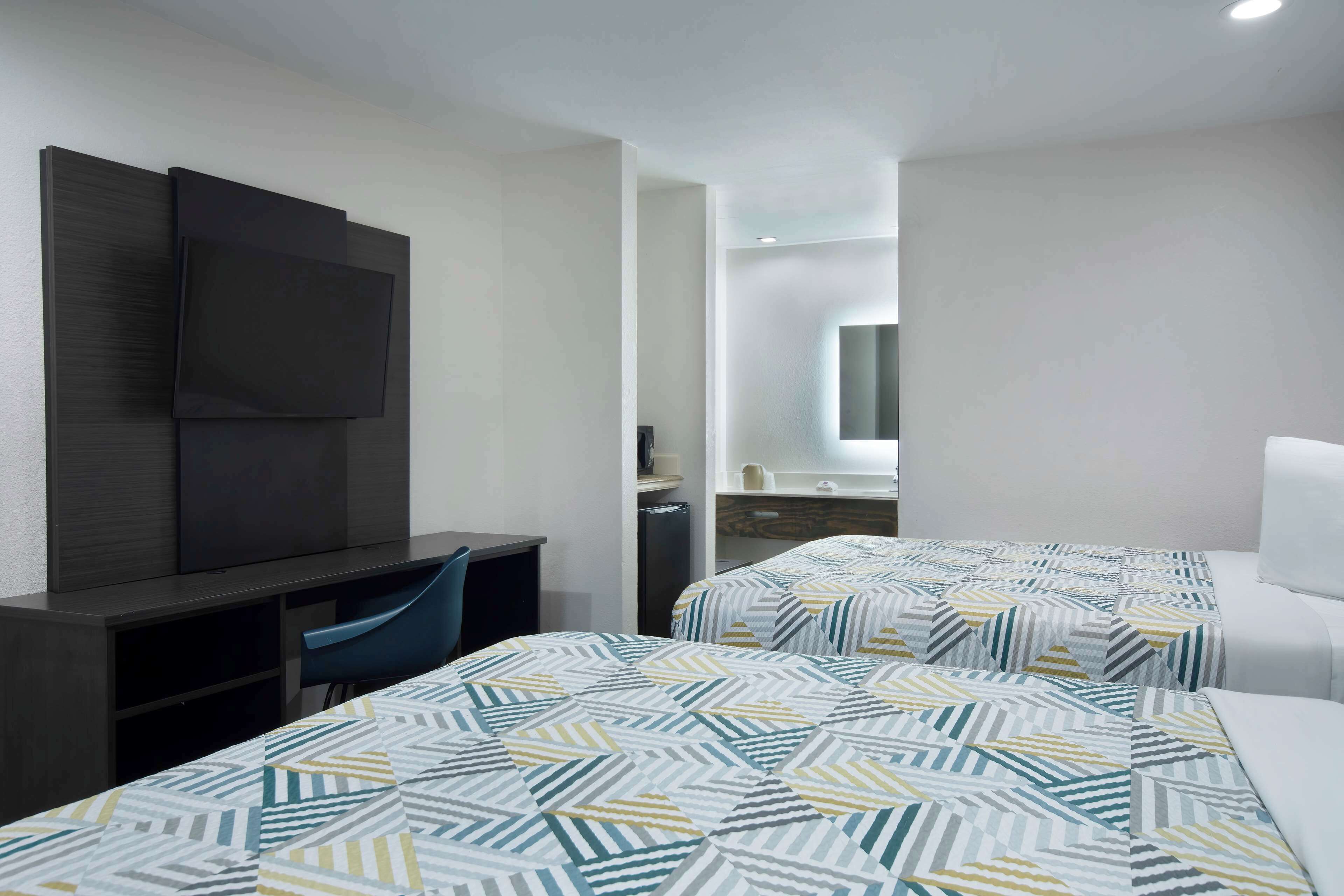 A hotel room with two beds, a desk, a chair, a TV, and a bathroom visible through an open door.