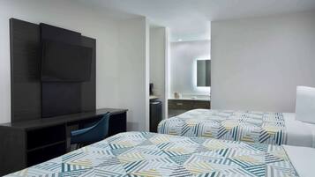 A hotel room with two beds, a desk, a chair, a TV, and a bathroom visible through an open door.