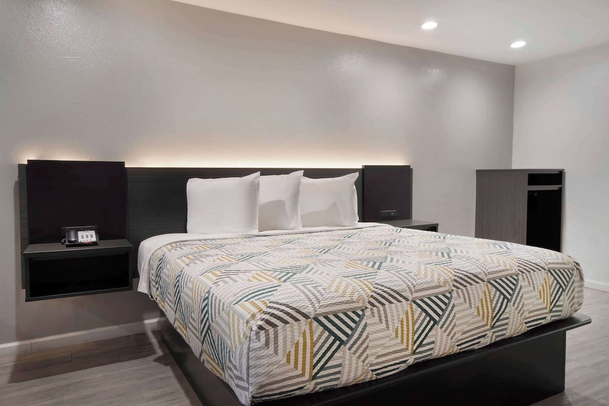 A modern hotel room with a large bed, a bedside table with a radio, a wardrobe, and a wall-mounted light fixture.