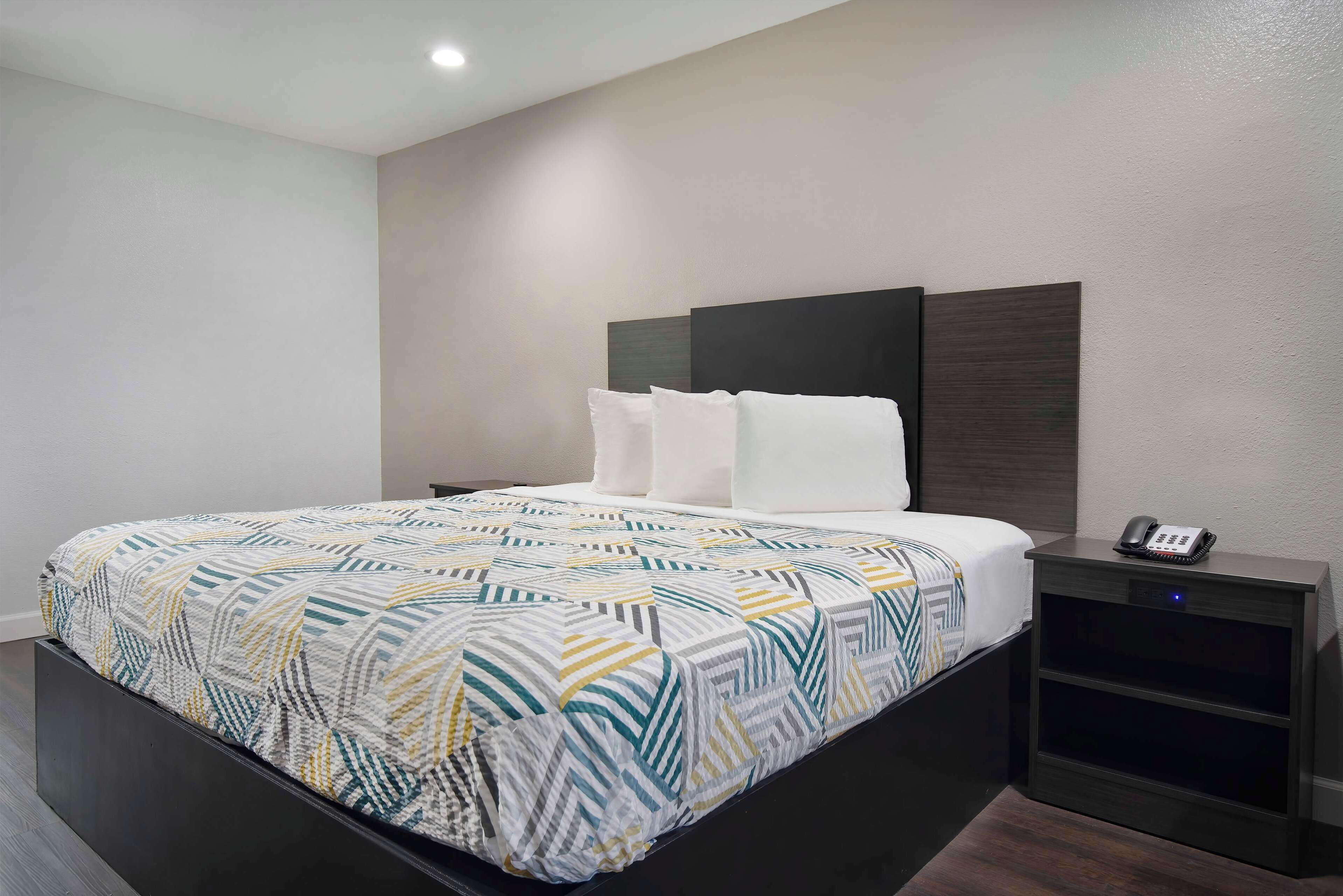 A modern hotel room with a bed, a bedside table with a phone, and a nightstand.
