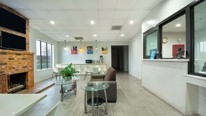 A modern kitchen with a brick fireplace, a dining area with a glass table and chairs, and a kitchen counter with a clock and a red cabinet. - Motel 6 Houston, TX - I-10 West (Houston)