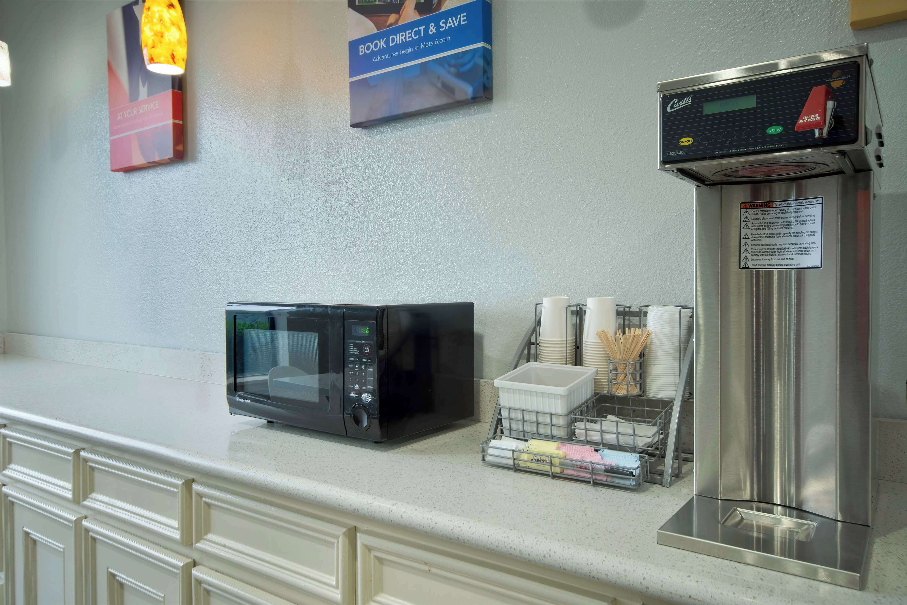 A kitchen counter with a microwave, a coffee machine, and a stack of disposable cups.
