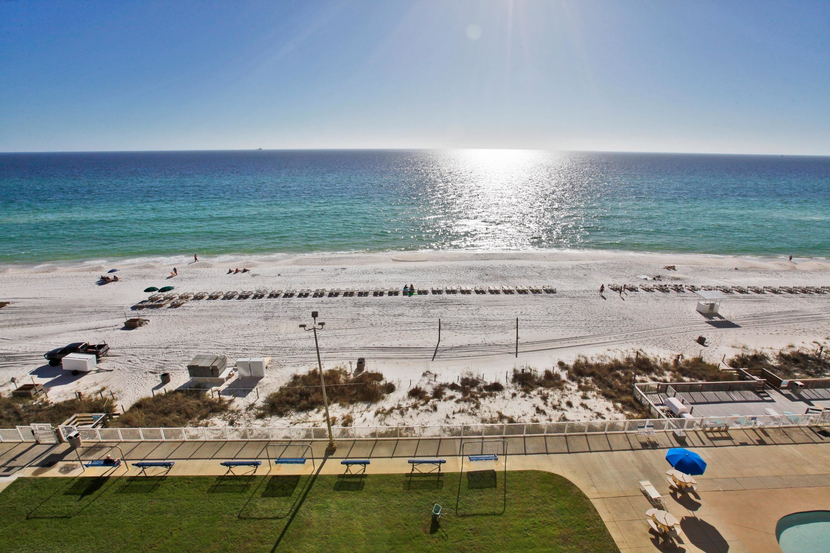 A beach with sunbathers, a volleyball court, and a pool area.
