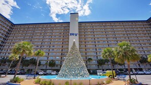 A hotel with a large building, a central fountain, and palm trees. - Regency Towers Beach Resort by Panhandle Getaways (Panama City Beach)